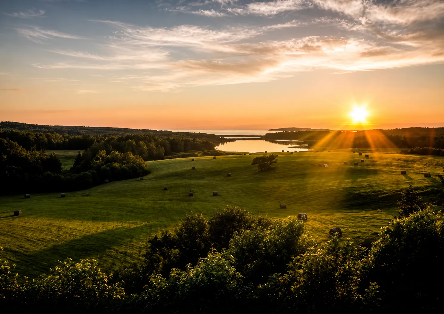 Hayfields sloping down to a calm ocean inlet at sunset near Little Judique, Cape Breton
